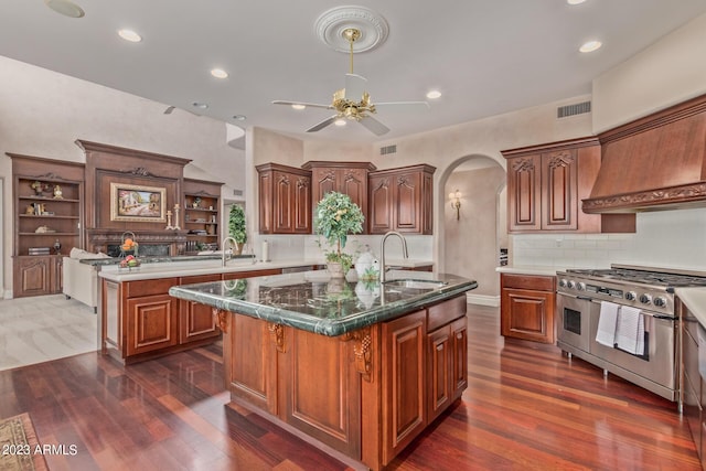 kitchen with arched walkways, visible vents, a kitchen island with sink, a sink, and double oven range