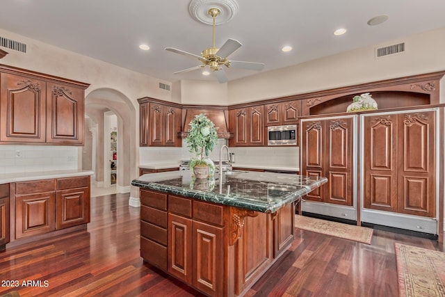 kitchen featuring arched walkways, visible vents, stainless steel microwave, and a sink