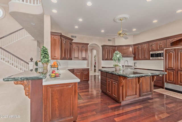 kitchen with arched walkways, stainless steel microwave, visible vents, dark wood-type flooring, and a sink