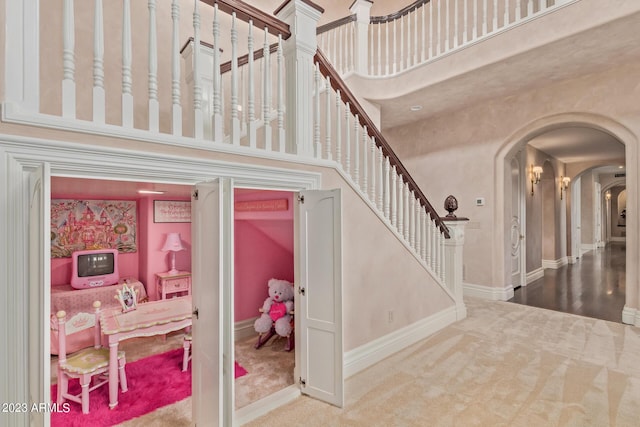 stairs with carpet floors, arched walkways, baseboards, and a high ceiling