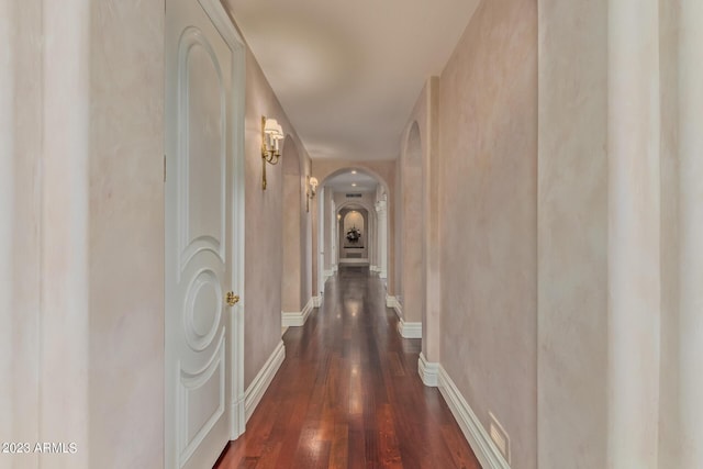 hallway featuring arched walkways, dark wood-type flooring, and baseboards