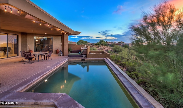 pool at dusk featuring a patio