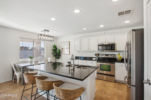 kitchen with decorative light fixtures, white cabinets, an island with sink, and appliances with stainless steel finishes