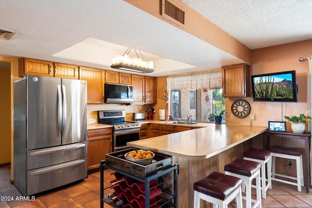 kitchen with sink, kitchen peninsula, a textured ceiling, a breakfast bar, and appliances with stainless steel finishes