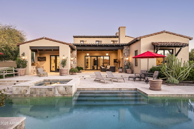 back house at dusk with a pool with hot tub and a patio