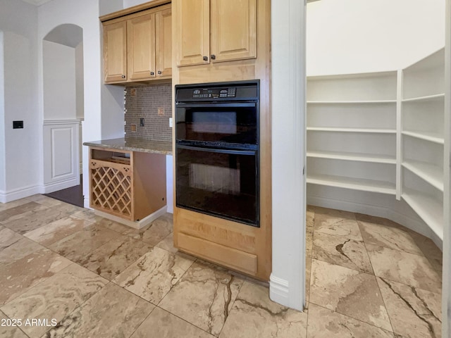 kitchen with stone counters, black double oven, decorative backsplash, and light brown cabinets