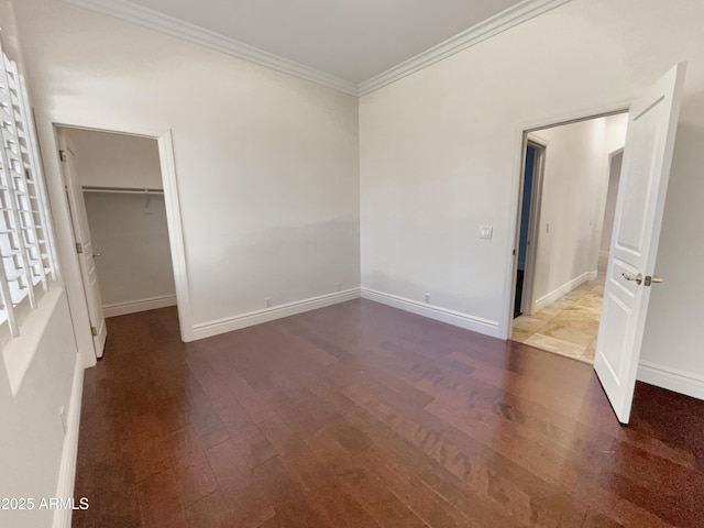 unfurnished bedroom with crown molding, a walk in closet, a closet, and dark wood-type flooring