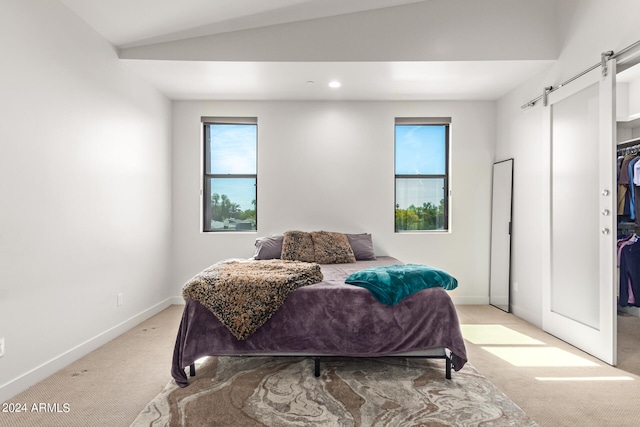 bedroom featuring lofted ceiling, a barn door, and light colored carpet