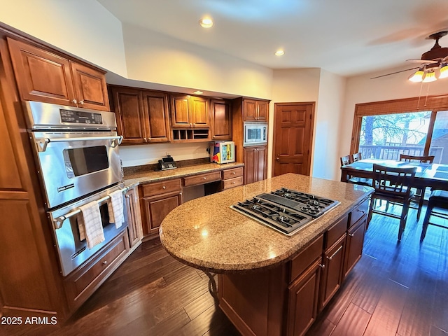 kitchen with light stone countertops, a ceiling fan, dark wood finished floors, appliances with stainless steel finishes, and a center island