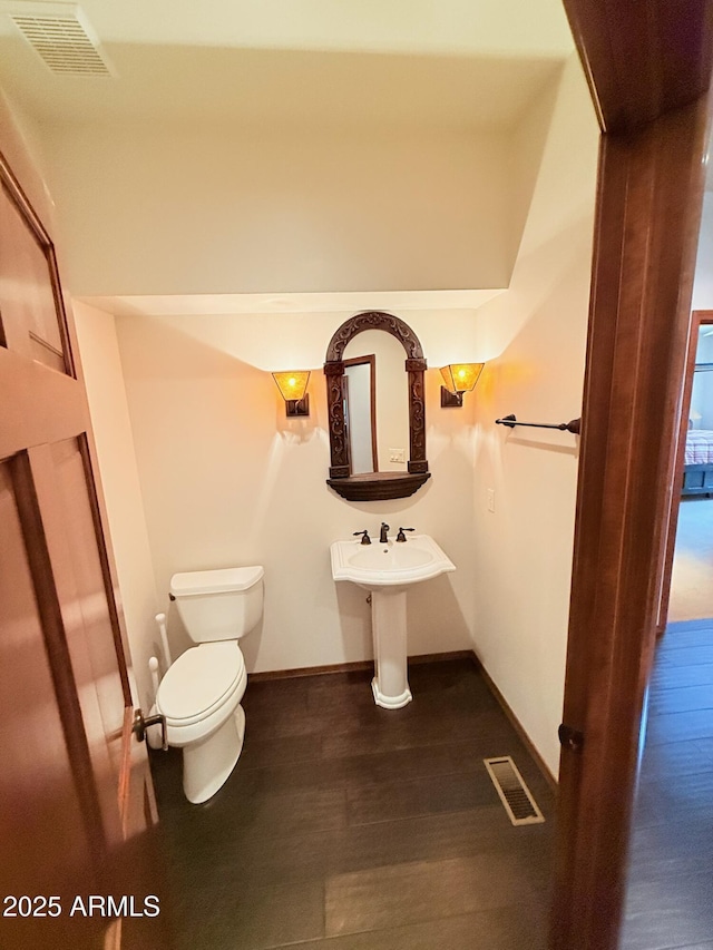 half bath featuring toilet, wood finished floors, baseboards, and visible vents