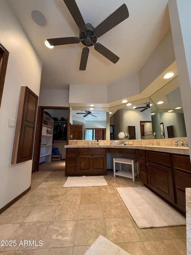 full bath with a spacious closet, vanity, baseboards, and ceiling fan