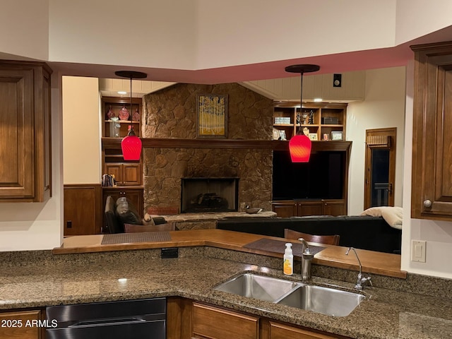 kitchen featuring a sink, hanging light fixtures, a stone fireplace, open floor plan, and dark stone counters