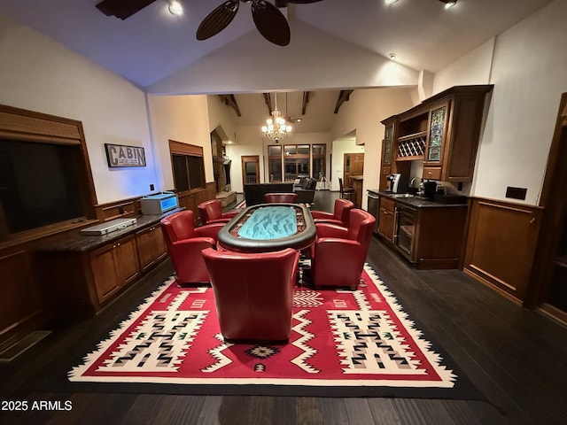 recreation room with bar area, high vaulted ceiling, ceiling fan with notable chandelier, dark wood finished floors, and wainscoting