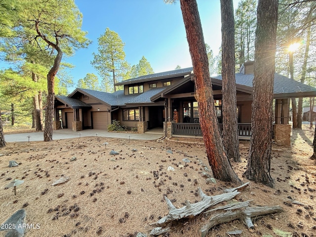 view of front of house featuring an attached garage, a shingled roof, a chimney, and covered porch