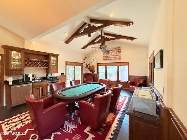 recreation room with a wainscoted wall, vaulted ceiling with beams, indoor wet bar, ceiling fan, and dark wood-type flooring