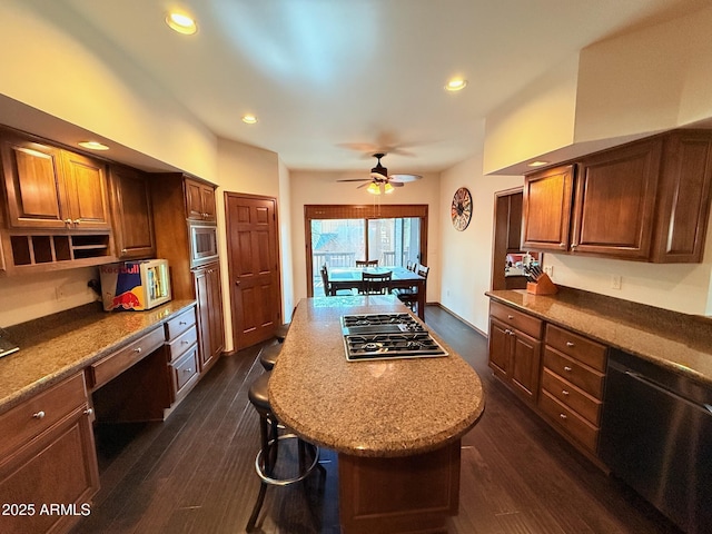kitchen with built in desk, ceiling fan, stainless steel appliances, dark wood finished floors, and a center island