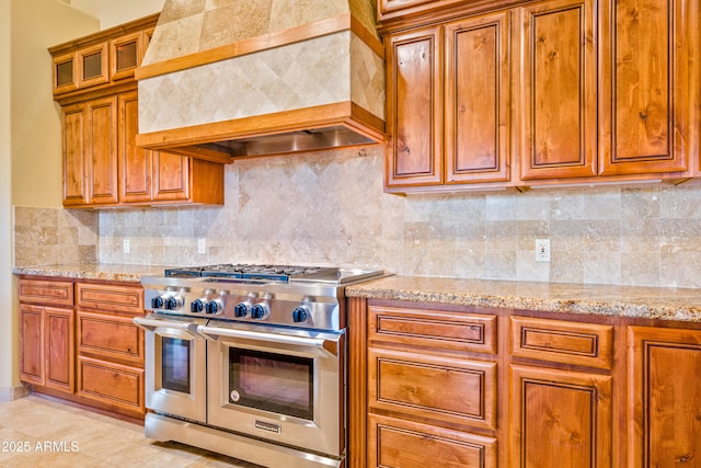 kitchen featuring range with two ovens, tasteful backsplash, custom range hood, and light stone counters