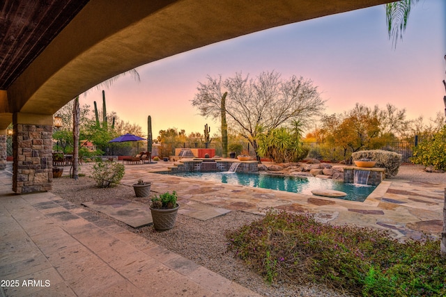 pool at dusk with a hot tub, a patio, and pool water feature