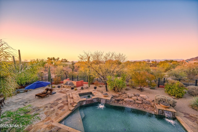 pool at dusk featuring a patio, pool water feature, and an in ground hot tub