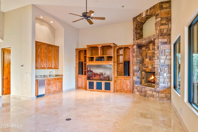 unfurnished living room with a stone fireplace, a towering ceiling, and ceiling fan