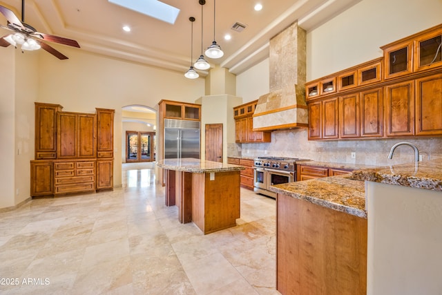 kitchen with a skylight, custom exhaust hood, high end appliances, hanging light fixtures, and a center island