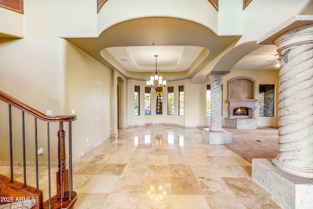 interior space featuring ornate columns, a raised ceiling, and ceiling fan with notable chandelier