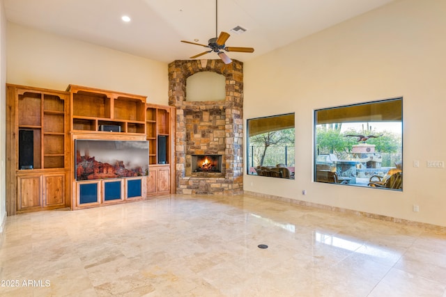 unfurnished living room featuring a stone fireplace, ceiling fan, and a towering ceiling