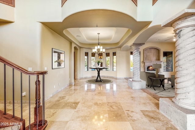 interior space featuring a chandelier, a raised ceiling, and ornate columns