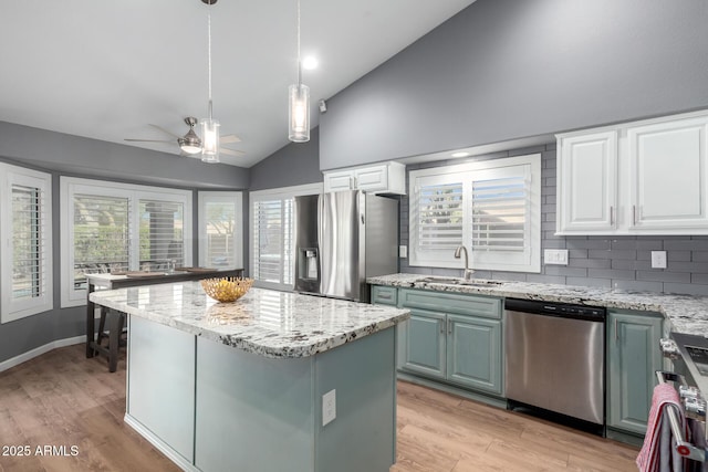 kitchen featuring light wood finished floors, lofted ceiling, appliances with stainless steel finishes, a center island, and a sink