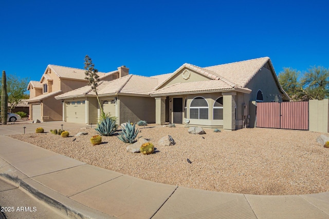 view of front of home featuring concrete driveway, a tile roof, an attached garage, a gate, and stucco siding