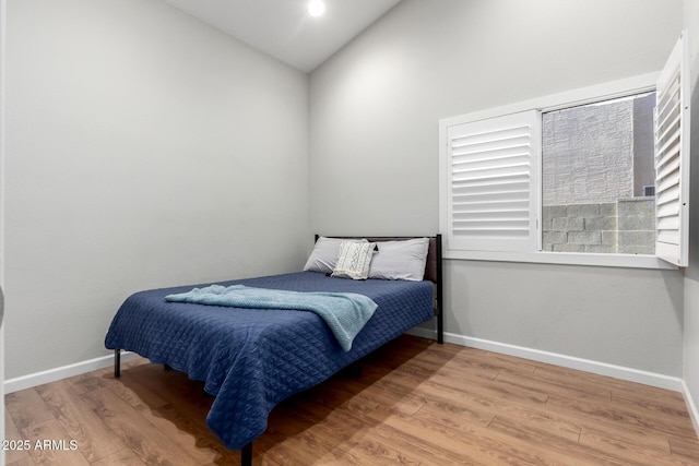 bedroom featuring lofted ceiling, baseboards, and wood finished floors