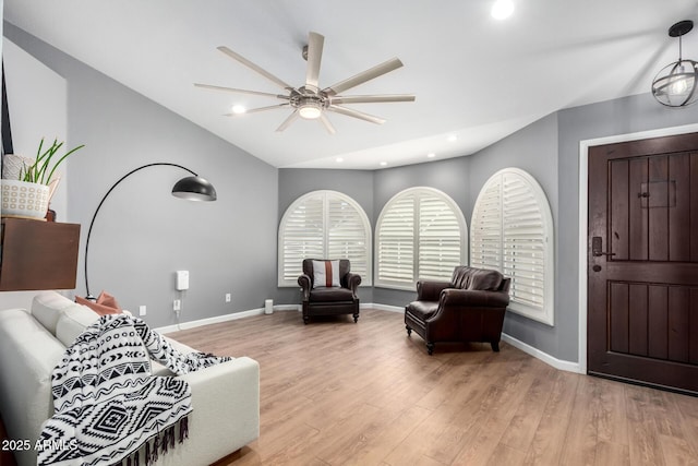 living area featuring lofted ceiling, light wood-style flooring, baseboards, and ceiling fan