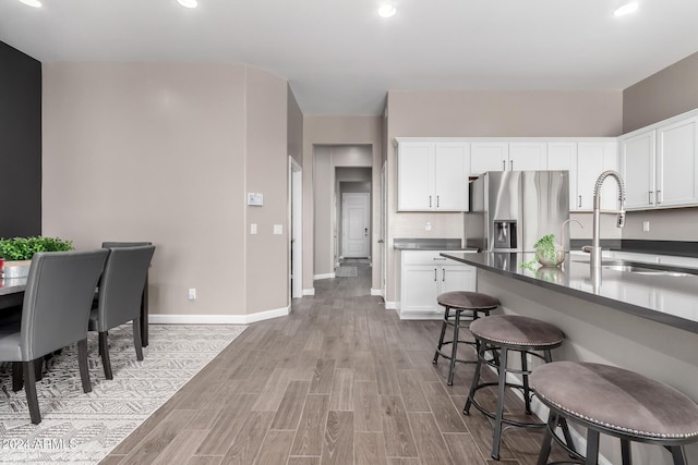 kitchen with white cabinets, stainless steel fridge with ice dispenser, a breakfast bar, and light hardwood / wood-style flooring