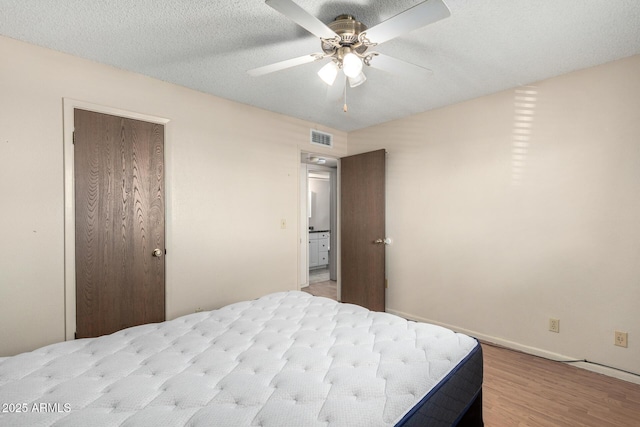 bedroom featuring a textured ceiling, wood finished floors, visible vents, a ceiling fan, and a closet