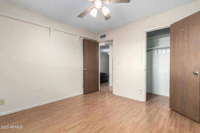 unfurnished bedroom featuring a textured ceiling, a closet, visible vents, and light wood-style floors