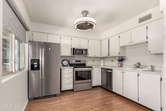 kitchen featuring a textured ceiling, a sink, appliances with stainless steel finishes, visible vents, and light countertops
