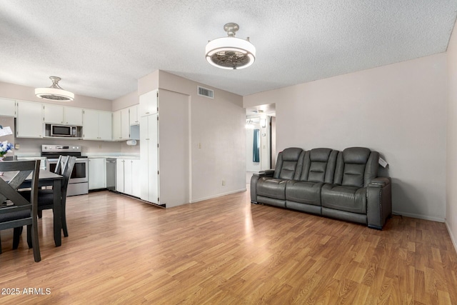 living room with baseboards, light wood-style flooring, visible vents, and a textured ceiling