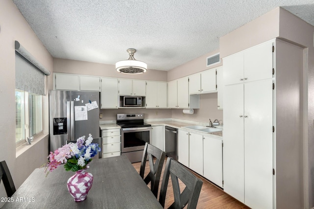 kitchen with a textured ceiling, a sink, visible vents, white cabinets, and appliances with stainless steel finishes