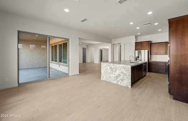 kitchen featuring sink, stainless steel appliances, tasteful backsplash, light stone counters, and a center island with sink