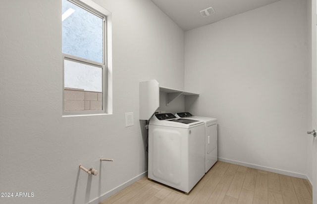 clothes washing area featuring washing machine and dryer, a wealth of natural light, and light hardwood / wood-style floors