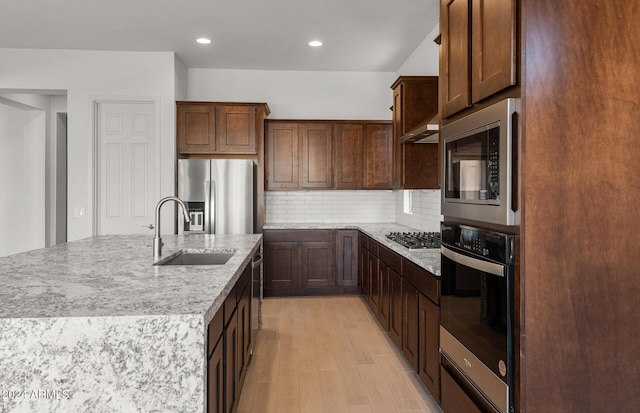 kitchen featuring backsplash, sink, stainless steel appliances, and an island with sink