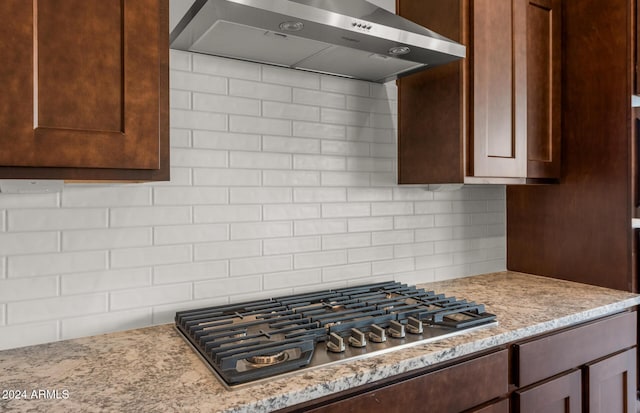 kitchen featuring decorative backsplash, wall chimney exhaust hood, light stone counters, and stainless steel gas cooktop