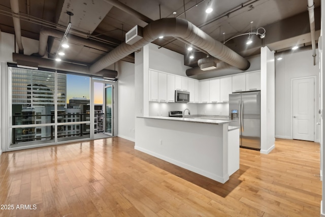 kitchen with white cabinets, a high ceiling, light wood-type flooring, and stainless steel appliances