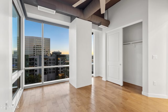 unfurnished bedroom featuring a wall of windows, light wood-type flooring, and a closet