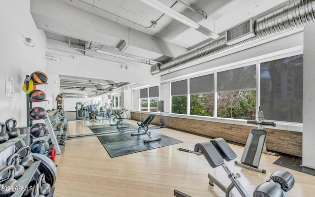 workout area with brick wall and light hardwood / wood-style flooring