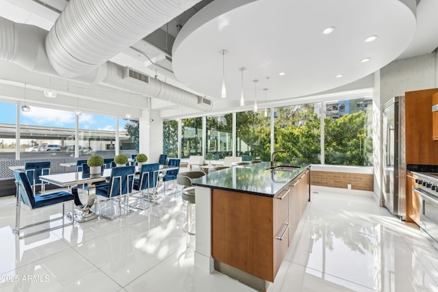 kitchen featuring a kitchen island with sink, sink, light tile patterned flooring, and decorative light fixtures