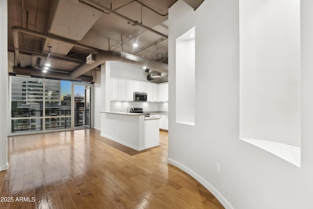 kitchen featuring light hardwood / wood-style flooring, a towering ceiling, white cabinetry, a wall of windows, and stainless steel appliances