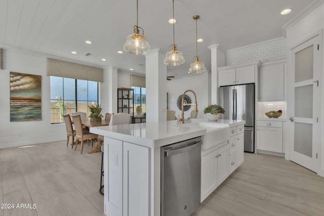 kitchen featuring stainless steel appliances, white cabinetry, sink, a kitchen island with sink, and decorative columns