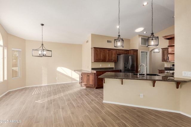 kitchen with a breakfast bar area, hanging light fixtures, kitchen peninsula, stainless steel fridge, and sink