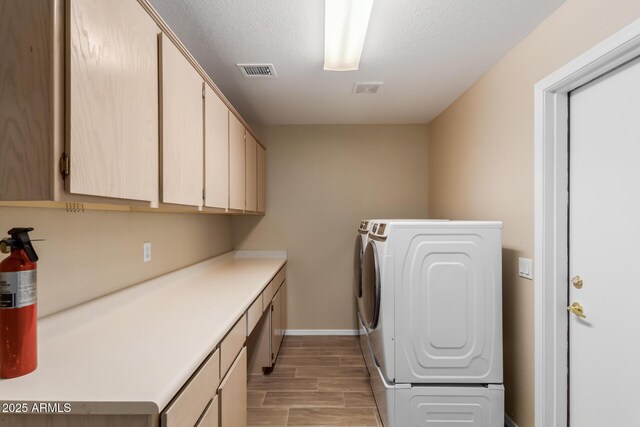 clothes washing area featuring washing machine and dryer, a textured ceiling, light hardwood / wood-style floors, and cabinets